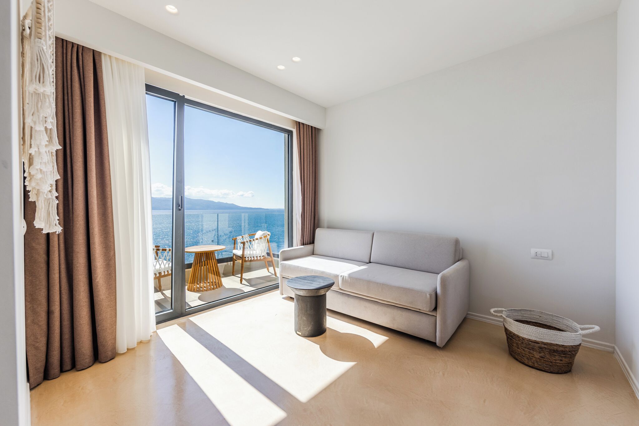 A modern living room with a sofa, a round coffee table, and a view of the sea through large windows.