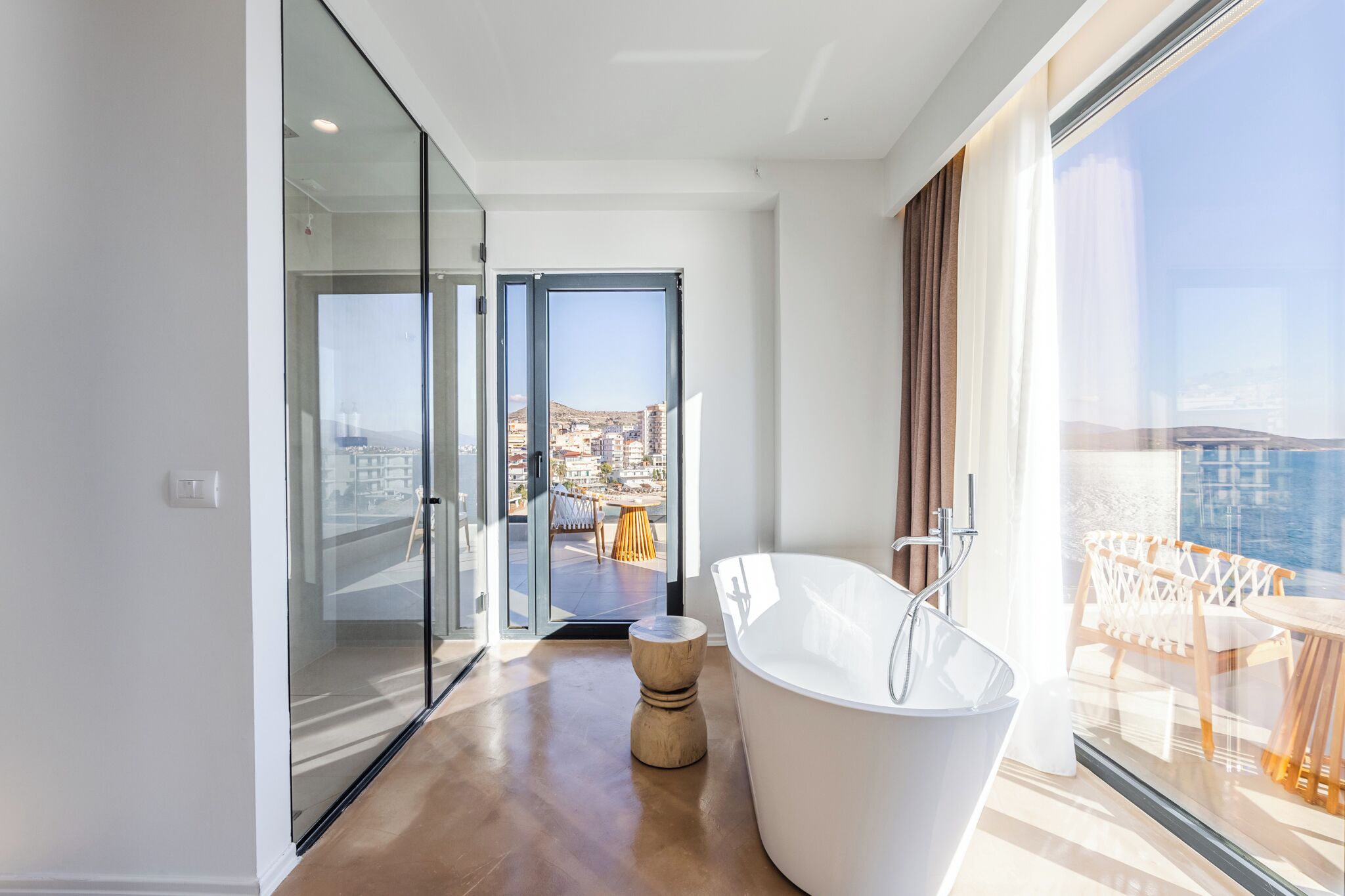 A modern bathroom with a freestanding bathtub, a glass door leading to a balcony, and a view of the city.