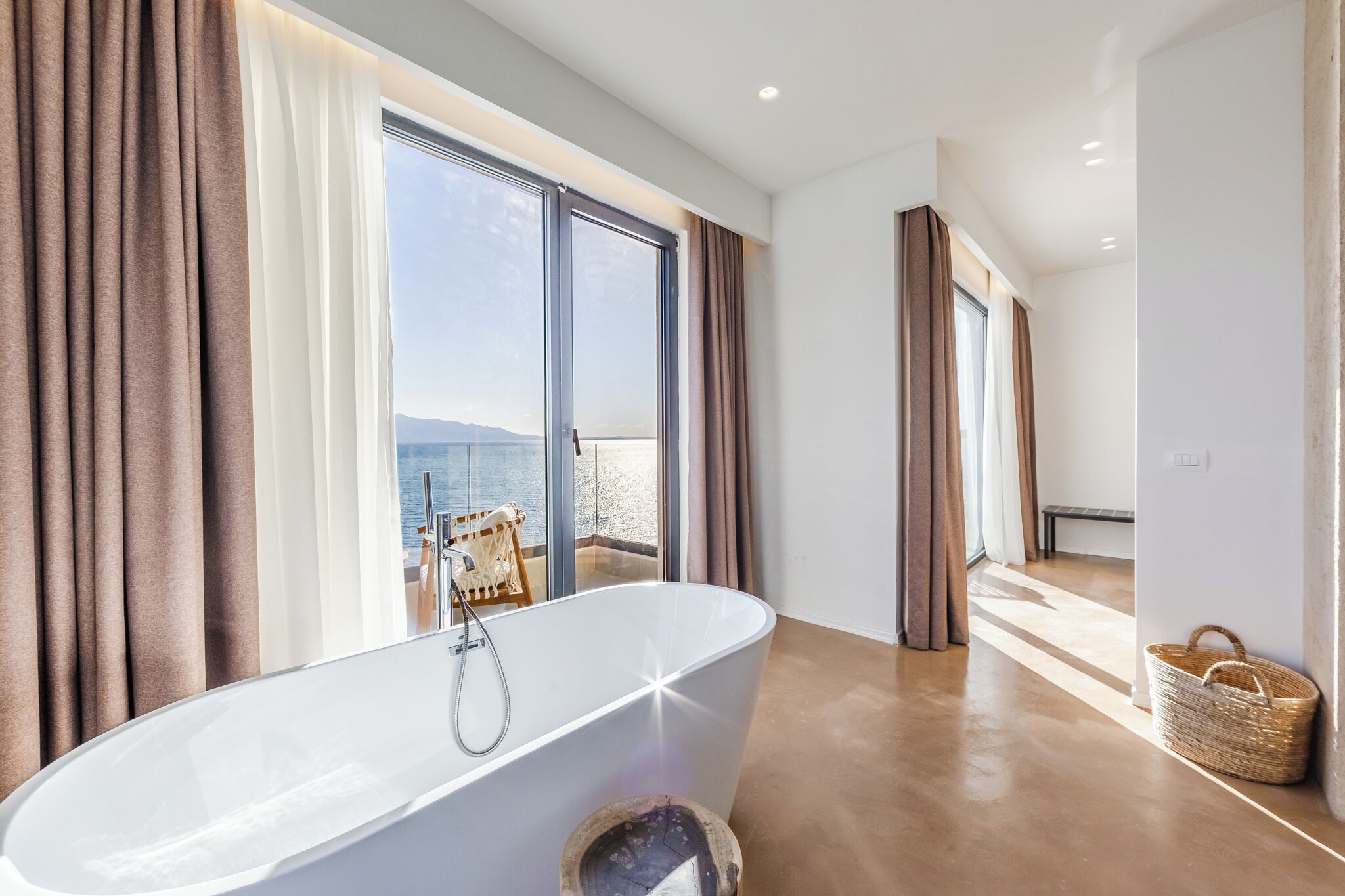 Ein modernes Badezimmer mit freistehender Badewanne, großen Fenstern und Meerblick.