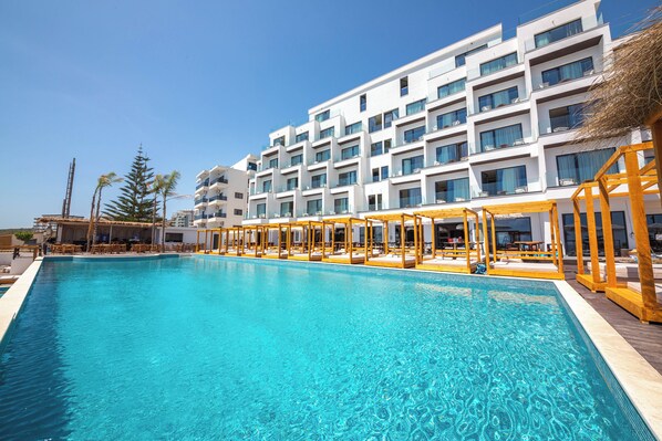 Une piscine avec des chaises longues et, au fond, un bâtiment doté de nombreux balcons.
