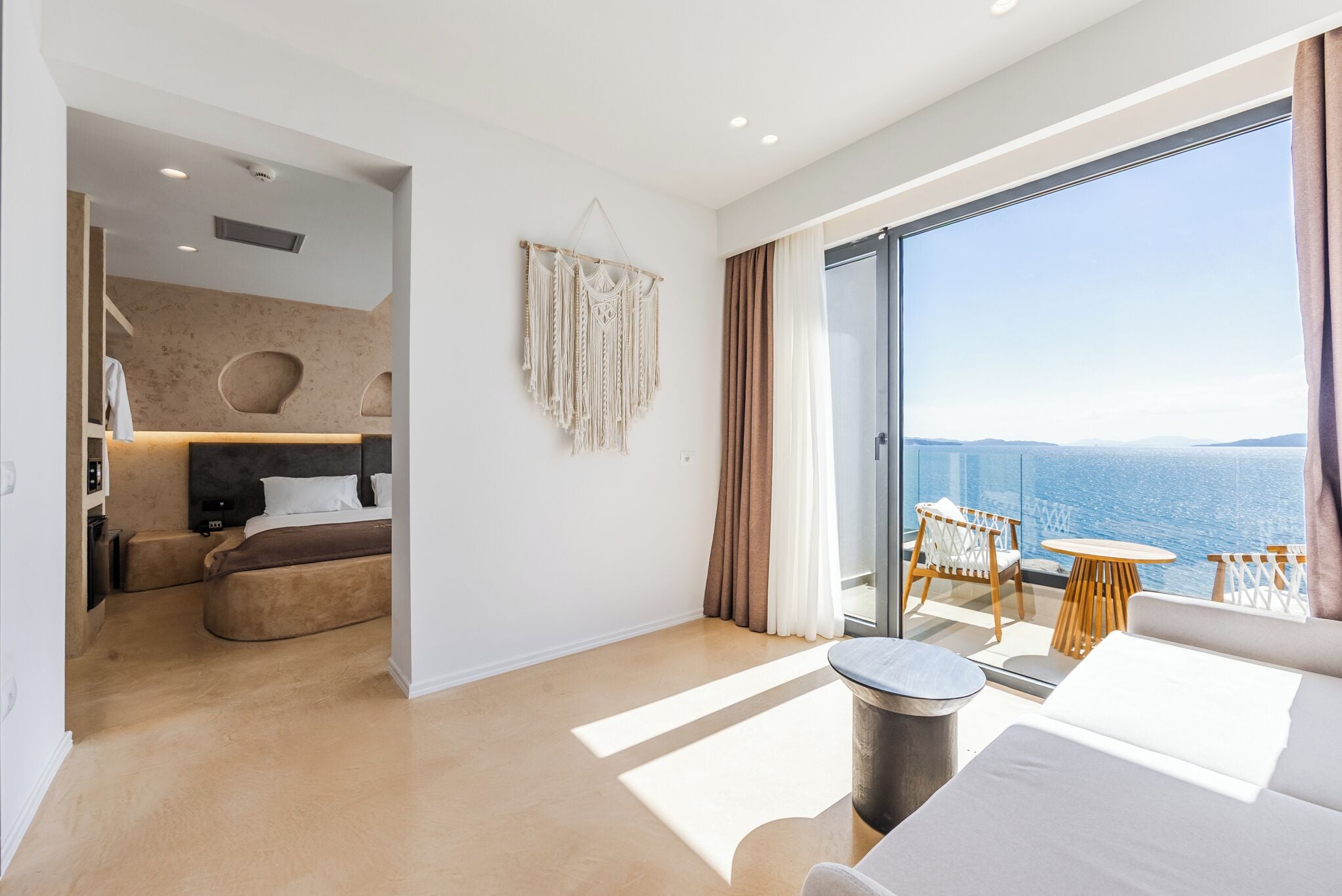 A modern hotel room with a large balcony, a cozy sitting area, and a view of the sea.