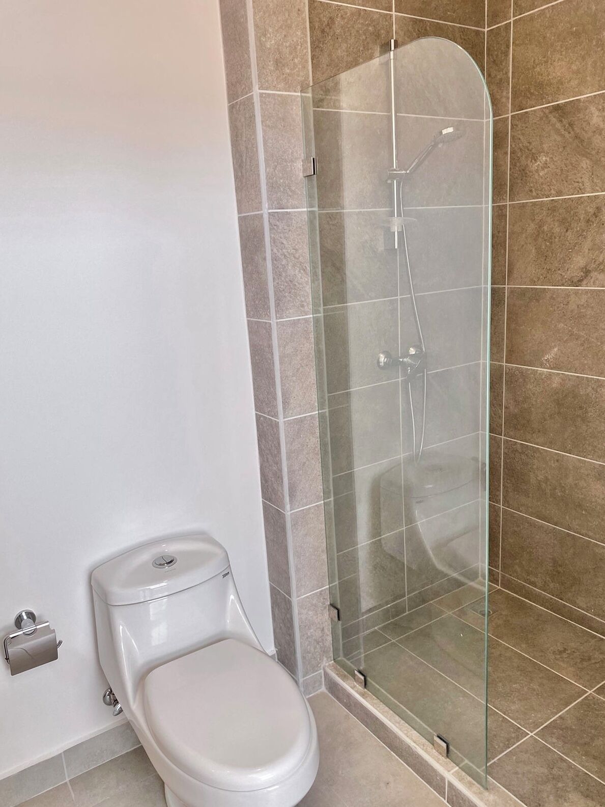Ein Badezimmer mit Toilette, einer Duschkabine und Fliesenwänden.