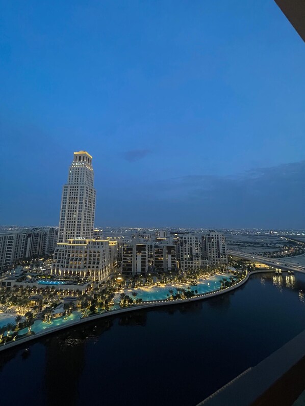 A high-rise building with "VIDA" illuminated on its facade, surrounded by other buildings and a waterfront area with pools and palm trees.