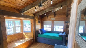A cozy cabin interior with wooden walls, a loft bed, a seating area, and a small table. - Family Friendly Log Cabin Nestled in Blue Ridge Foothills (Stuarts Draft)