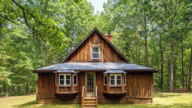 A rustic log cabin with a steep gabled roof, a central chimney, and a front porch with a set of stairs leading to the entrance. - Family Friendly Log Cabin Nestled in Blue Ridge Foothills (Stuarts Draft)
