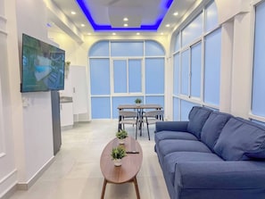 A modern living room with a flat-screen TV, a sofa, a coffee table, and a dining area with chairs and a small table. - Plaza Achim 7, Luxury Apt 250m From Sosua Beach! (Sosúa)