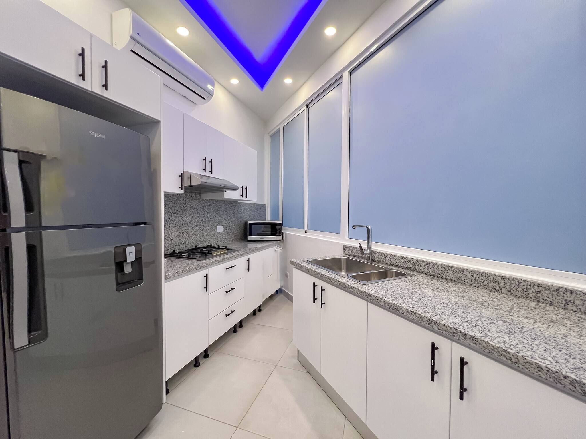 A modern kitchen with white cabinets, a stainless steel refrigerator, a microwave, and a double sink.