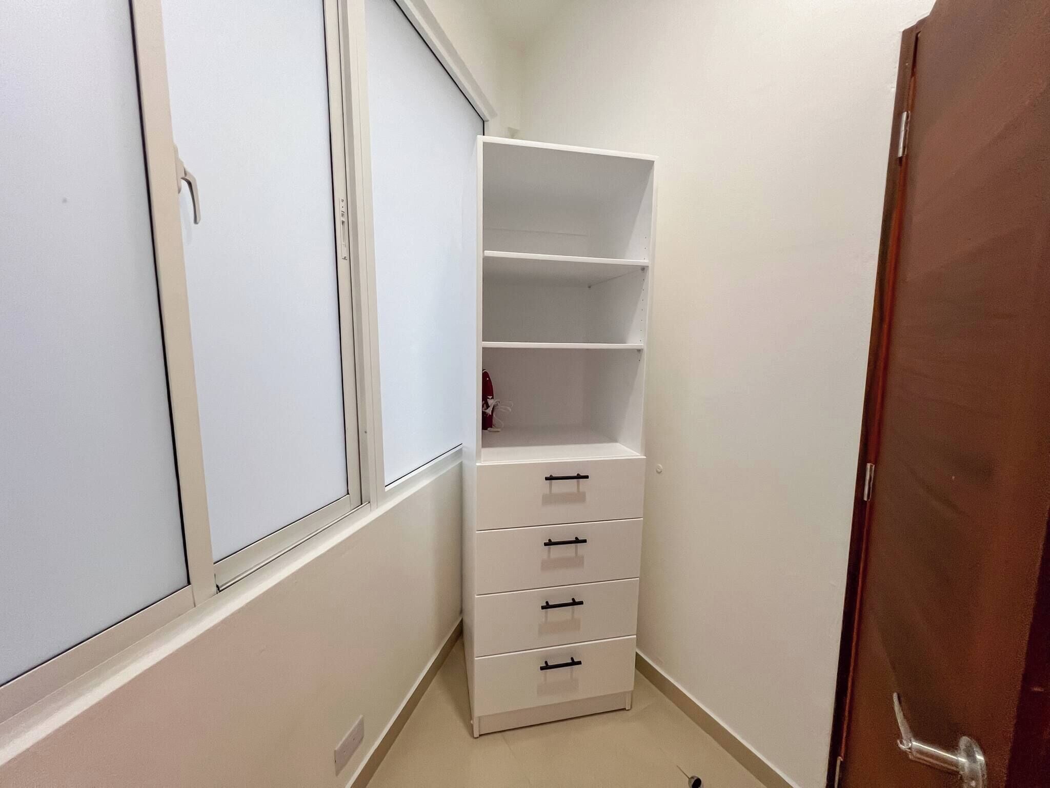 A narrow hallway with a white wardrobe, a wooden door, and a white shelf unit with drawers.