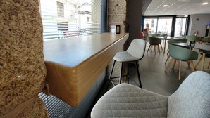 Un café moderno con mostrador de madera, taburetes de bar y vista a la calle a través de grandes ventanales.