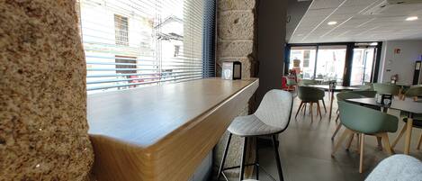 Un café moderno con mostrador de madera, taburetes de bar y vista a la calle a través de grandes ventanales.