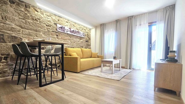 Una sala de estar con pared de piedra, un sofá amarillo, una mesa de centro y un comedor con sillas.