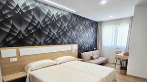Habitación de hotel con dos camas, un sofá, un escritorio y un papel tapiz estampado.
