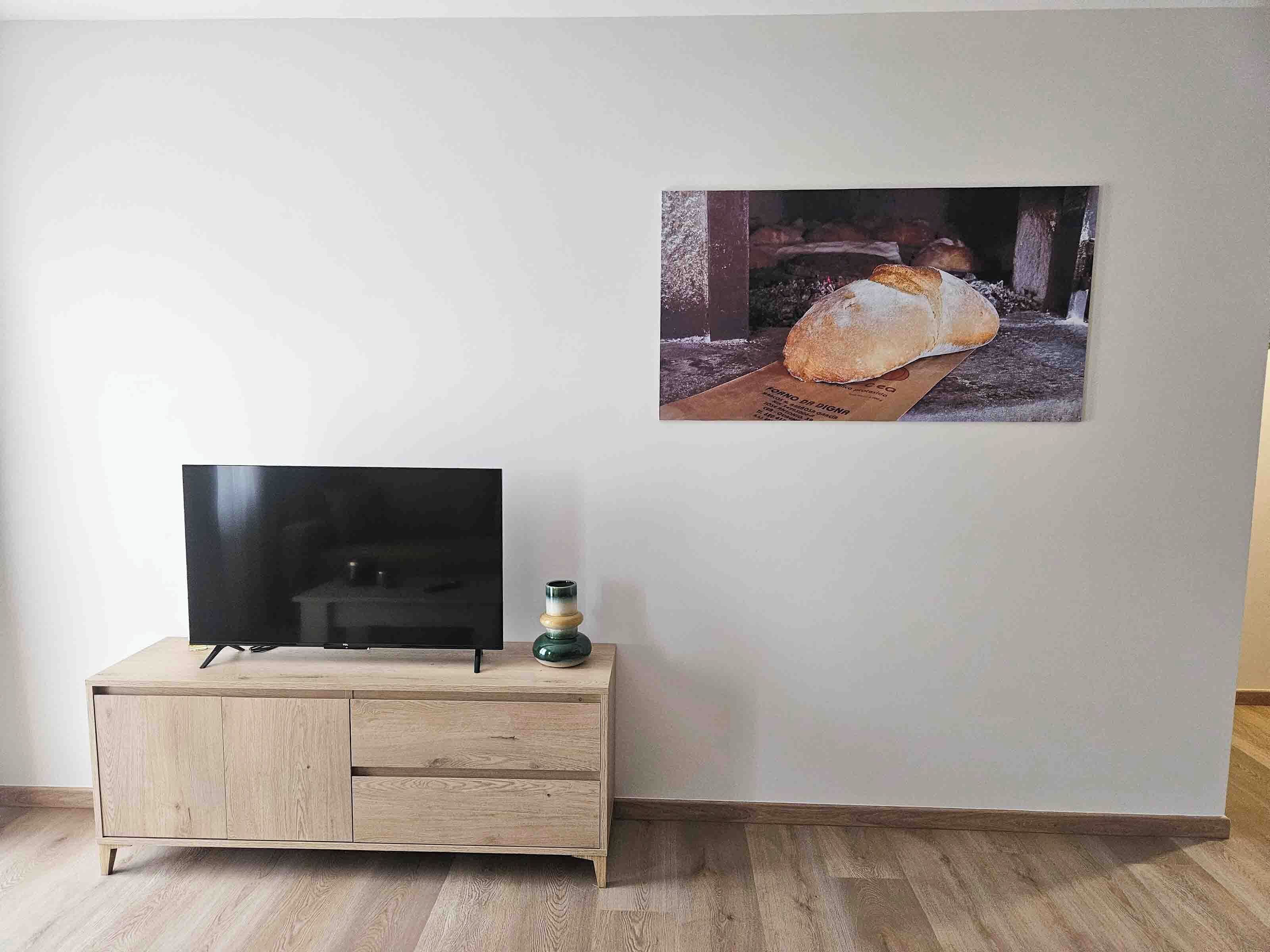 Una habitación con un armario de madera, un televisor de pantalla plana y un cuadro con una hogaza de pan en la pared.