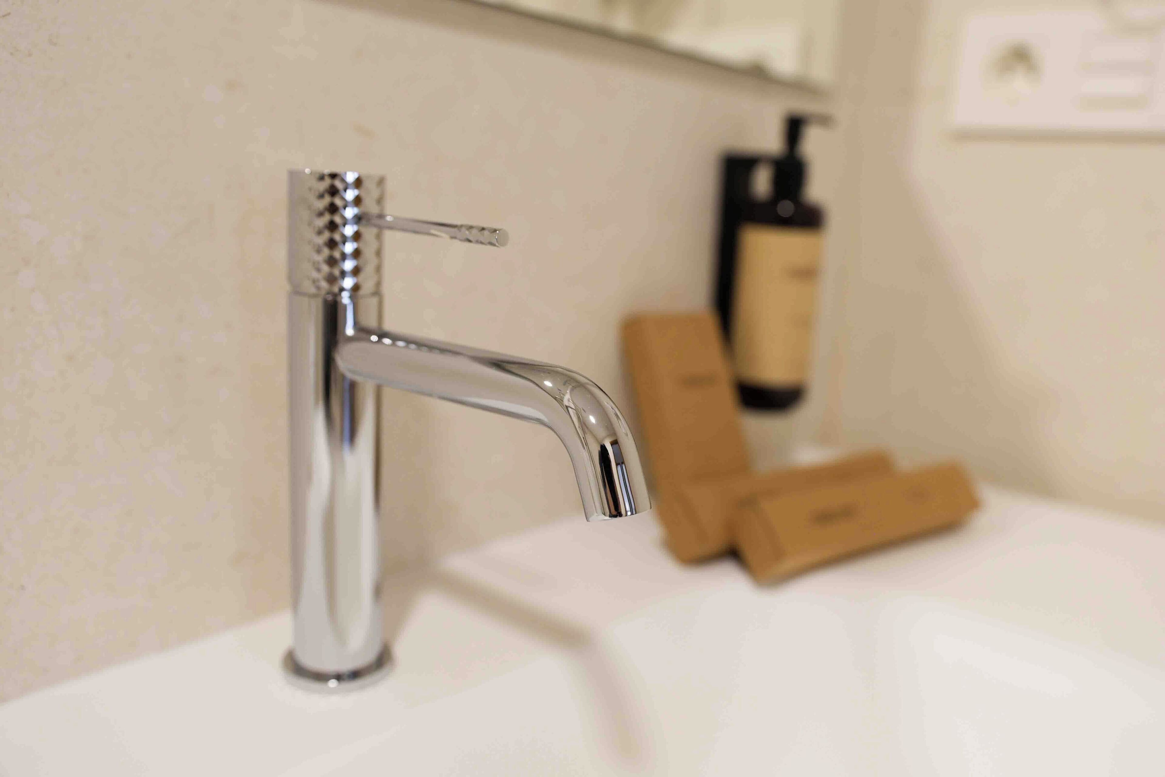 A modern bathroom with a chrome faucet, a white sink, and a bottle of hand soap on the counter.