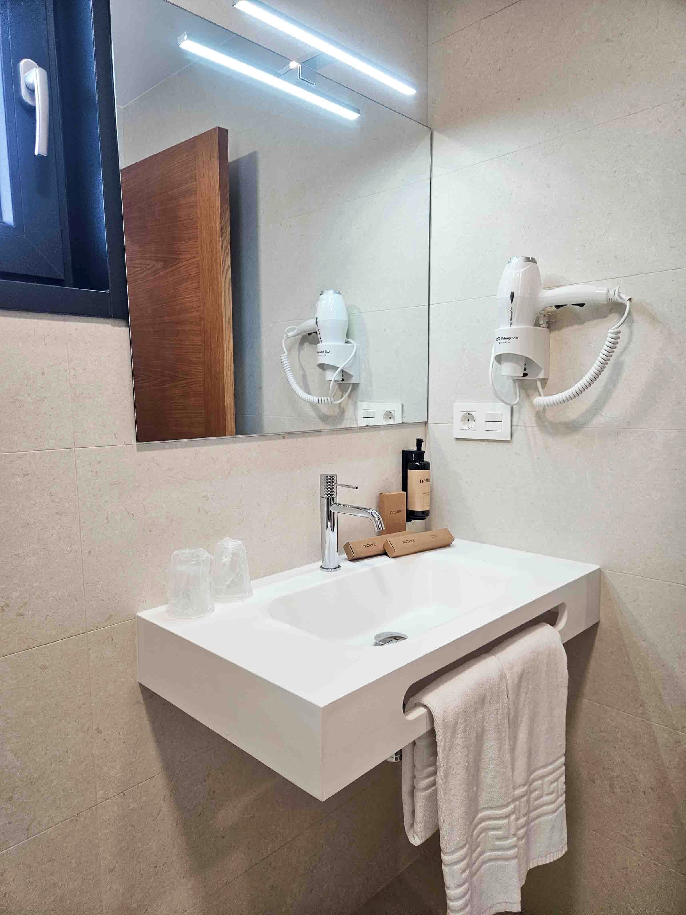 Un baño moderno con lavamanos blanco, espejo, secador de pelo y toalla.