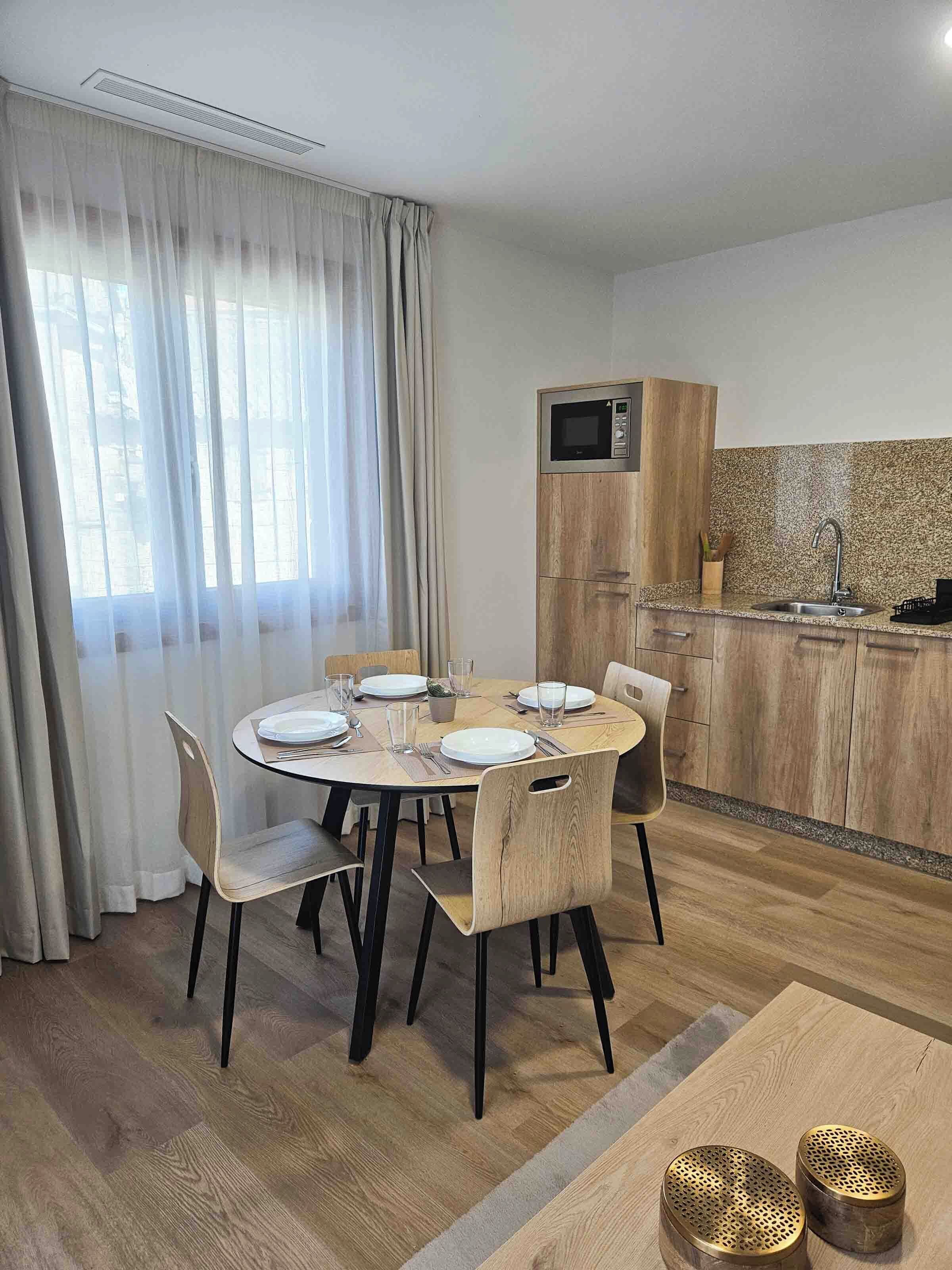 A modern kitchen with a microwave, sink, and wooden cabinets. There is a dining area with a round table and chairs.