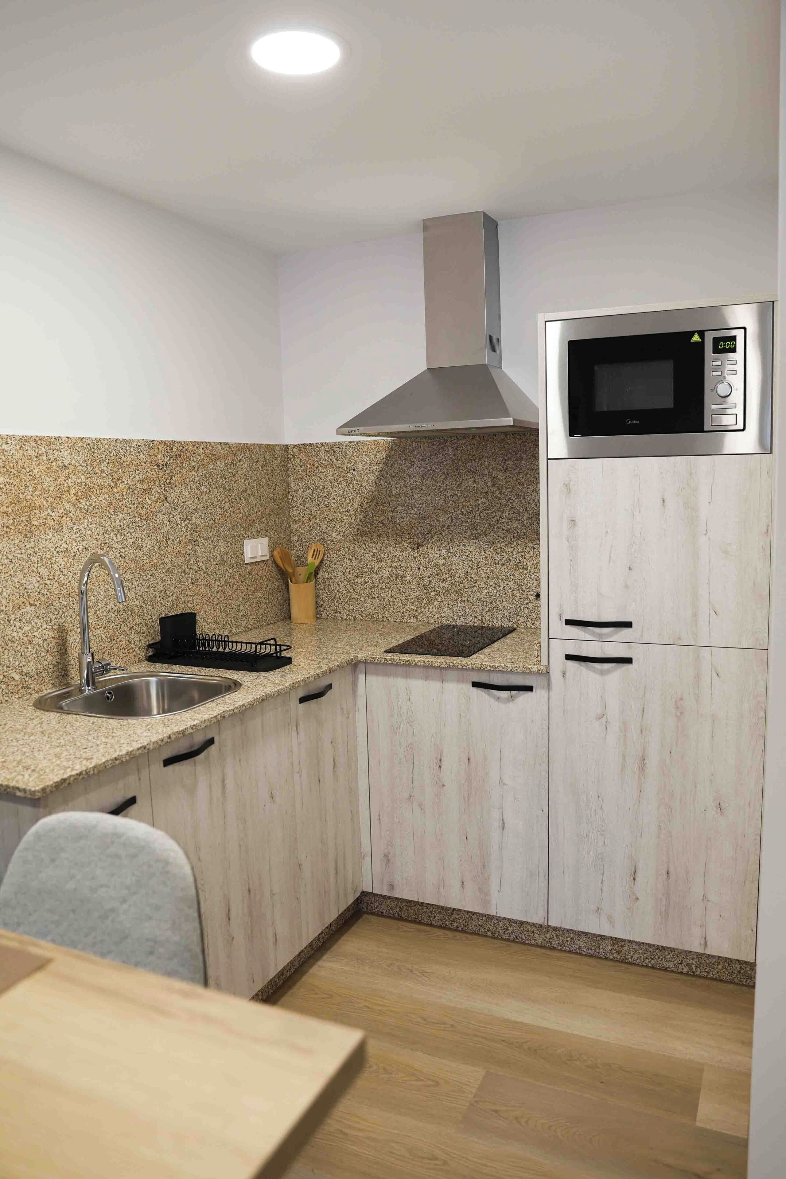 Una cuina compacta amb encimera de granit, electrodomèstics d'acer inoxidable i armaris de fusta clara.