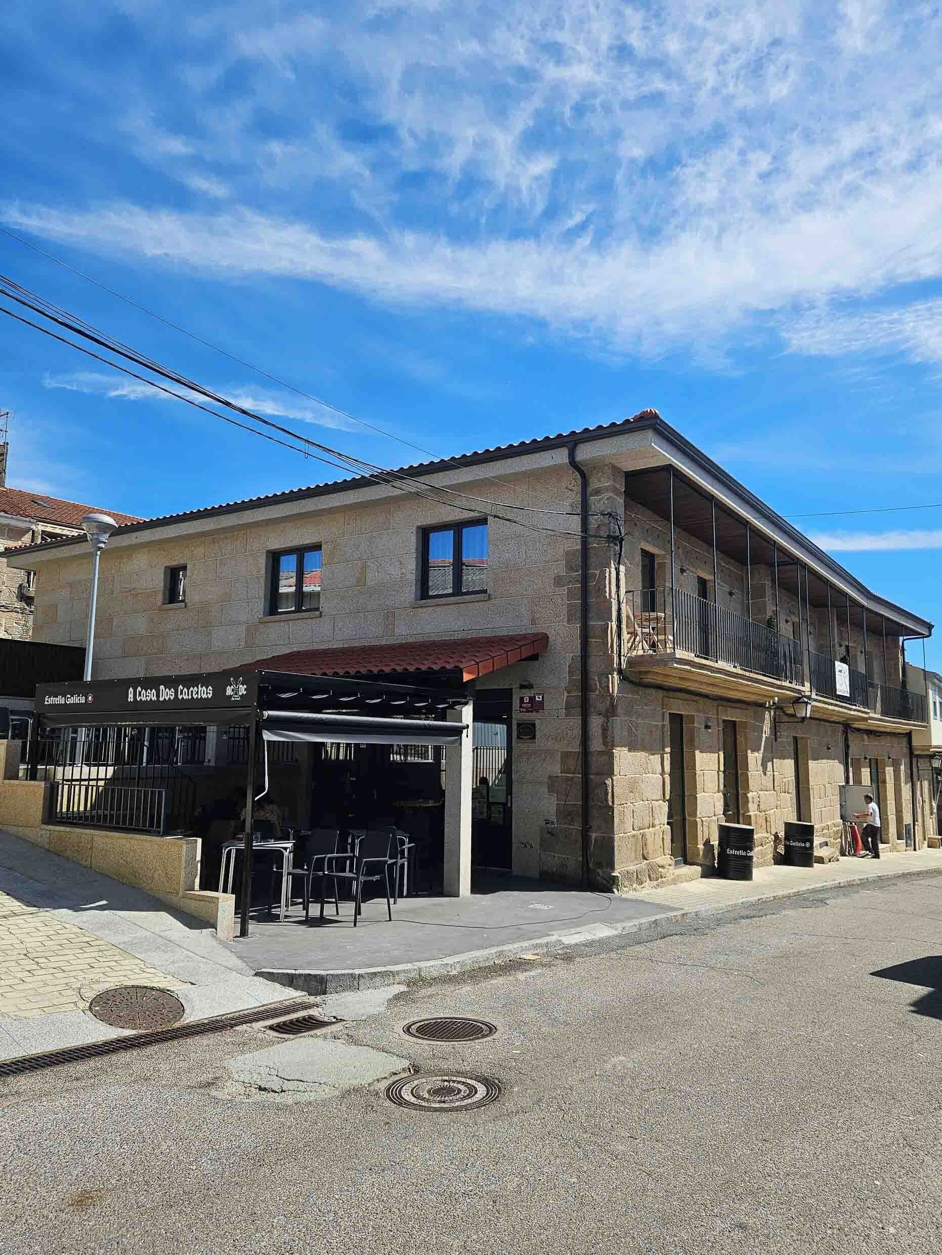 Un bâtiment à deux étages avec une façade en pierre, un espace extérieur couvert aménagé en coin salon et une enseigne indiquant « A Casa Dos Caretes ».