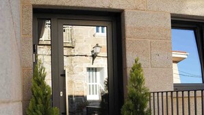Entrada de un edificio con una puerta oscura, dos macetas y un muro de piedra.