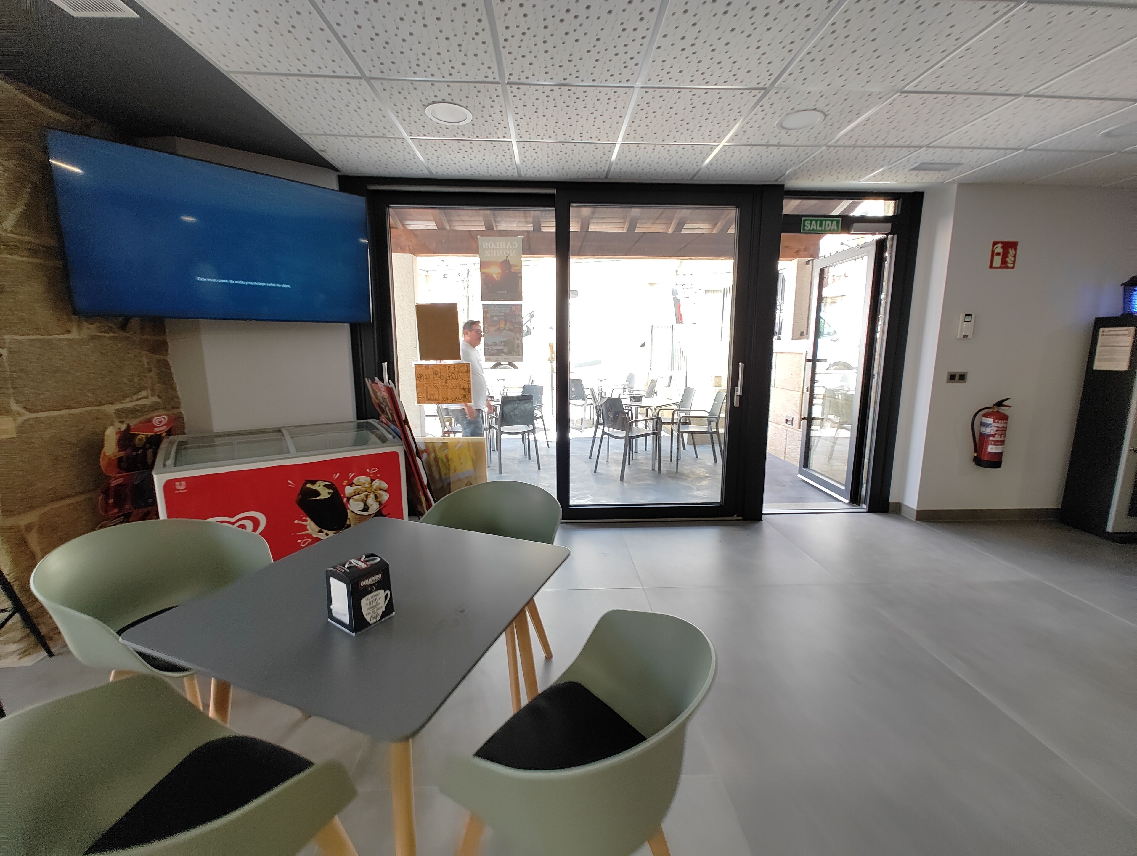 A modern interior with a flat-screen TV mounted on the wall, a table with chairs, and a glass door leading outside.