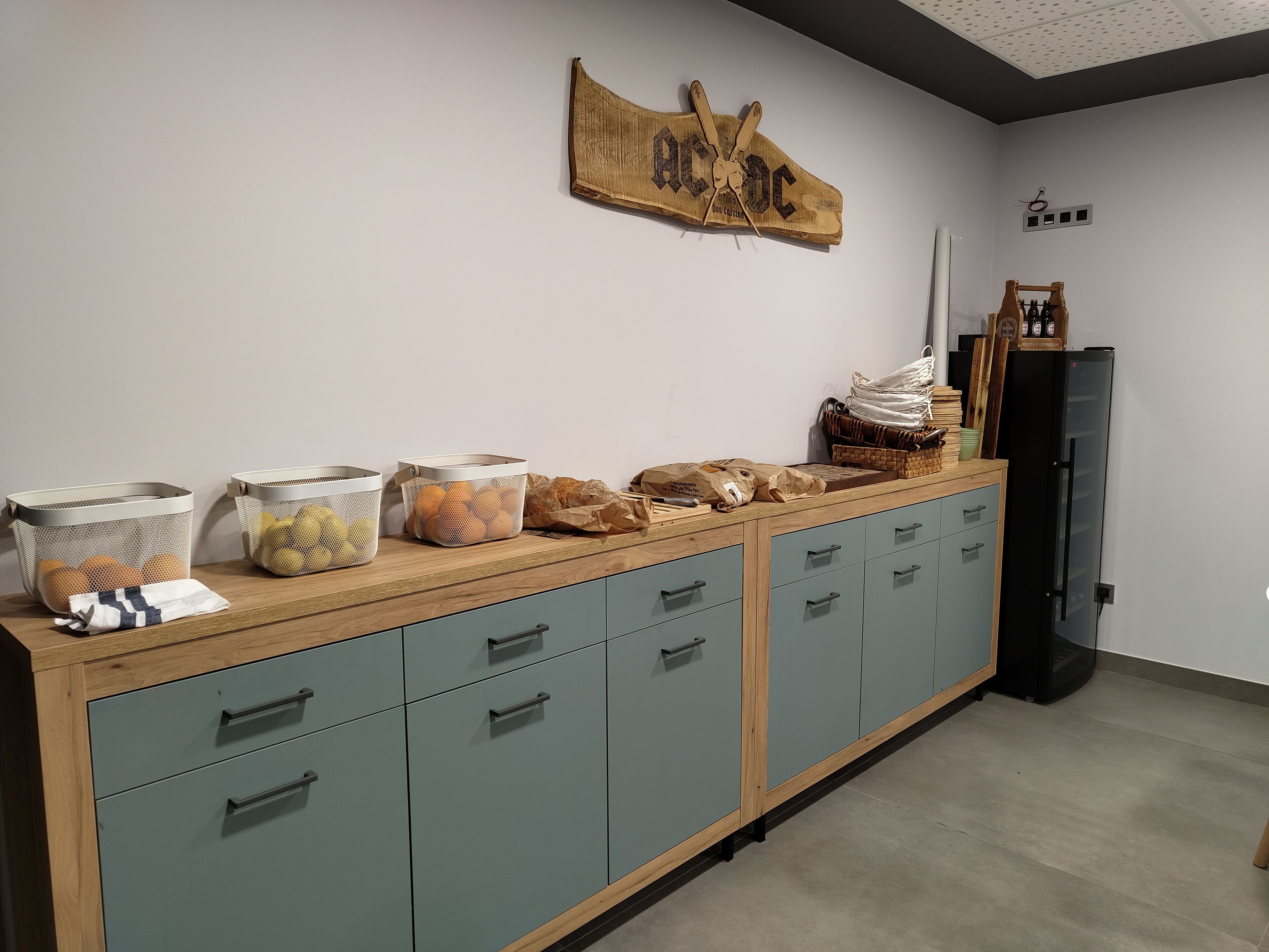 A kitchenette with a wooden countertop, a black refrigerator, and a wall-mounted wooden sign.