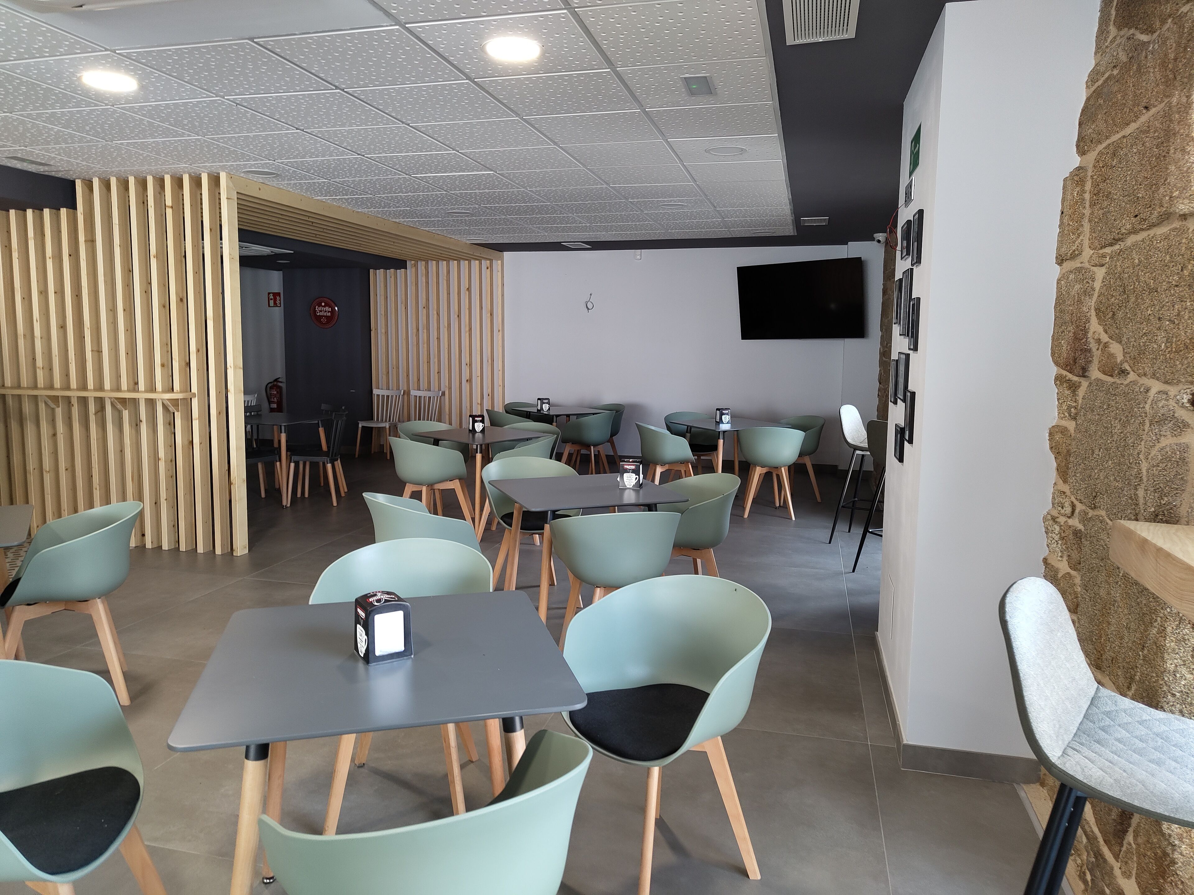 A modern dining area with multiple tables and chairs, a fire extinguisher, and a mounted television on the wall.