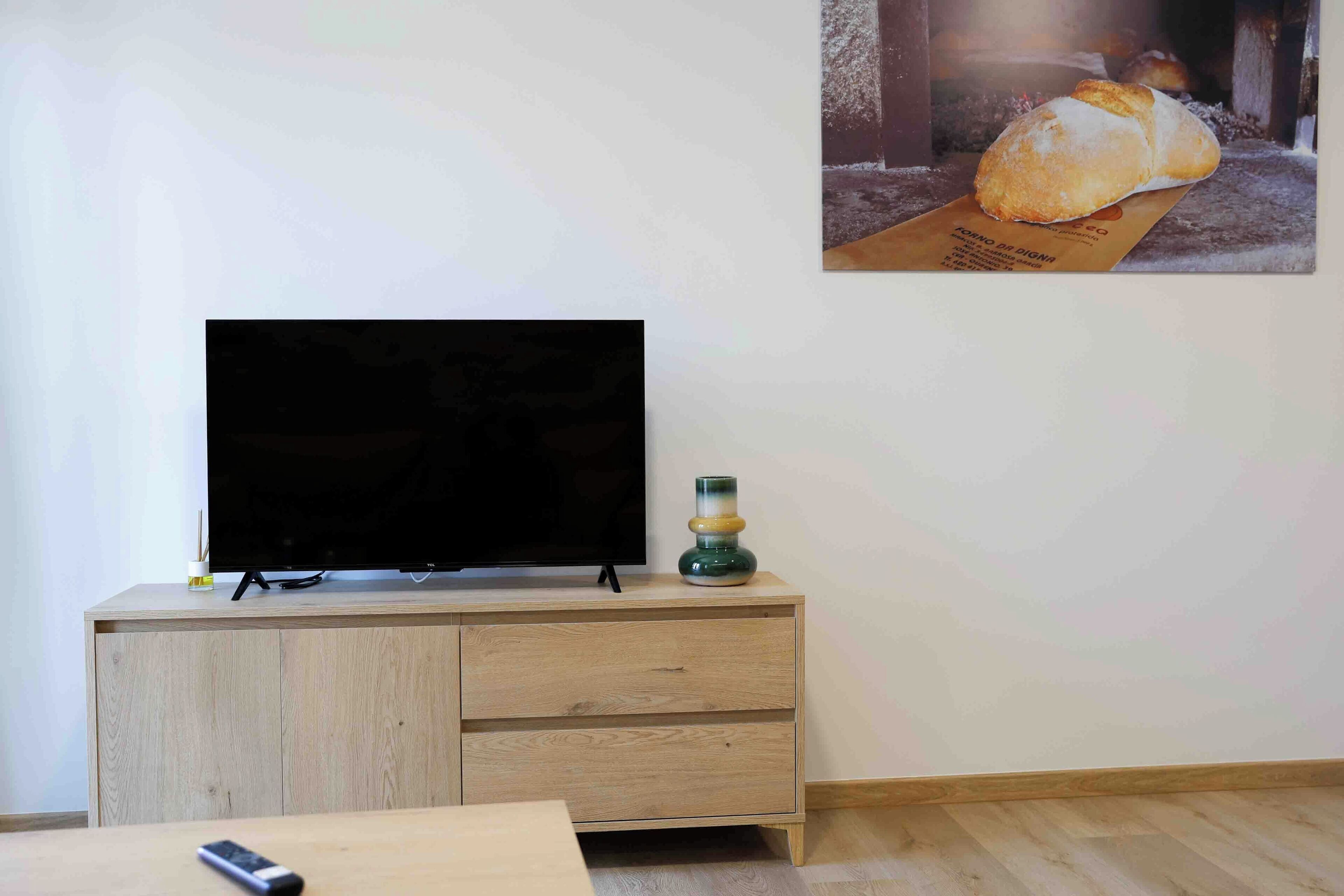 A living room with a wooden cabinet, a television, and a painting of bread on the wall.