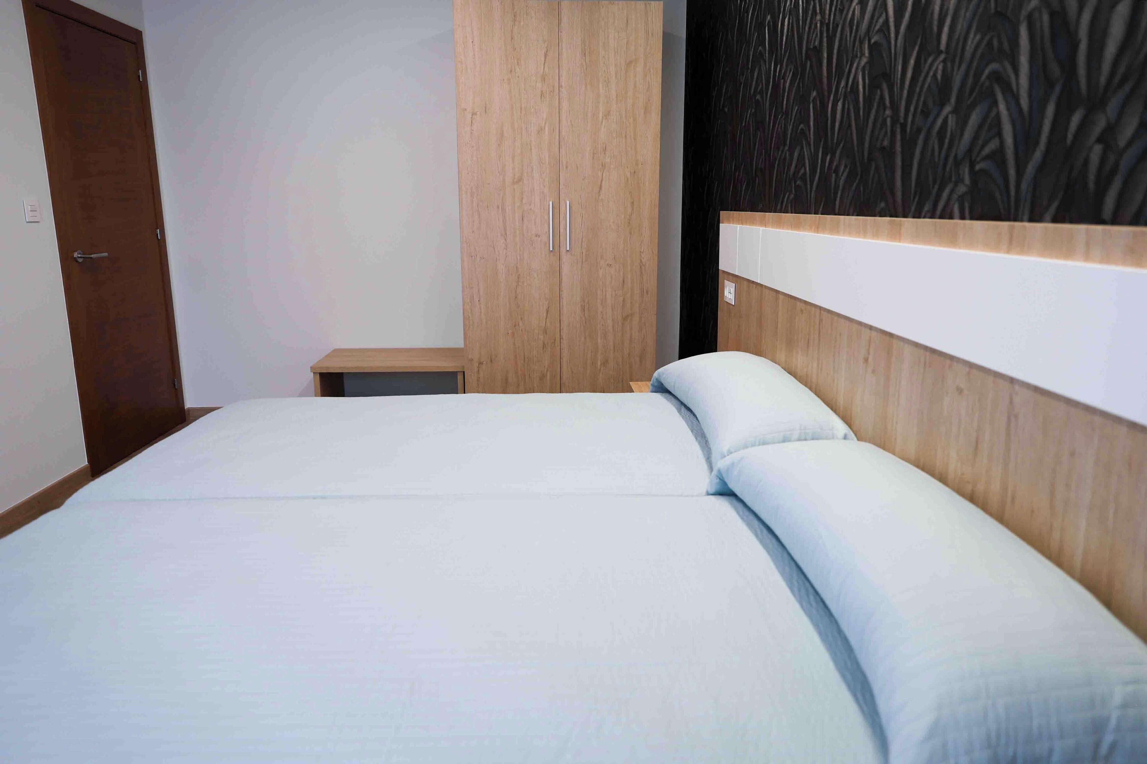 A bedroom with a bed, a wooden wardrobe, and a small bedside table.