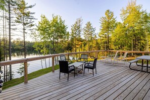 A wooden deck with outdoor furniture, overlooking a lake and surrounded by trees.