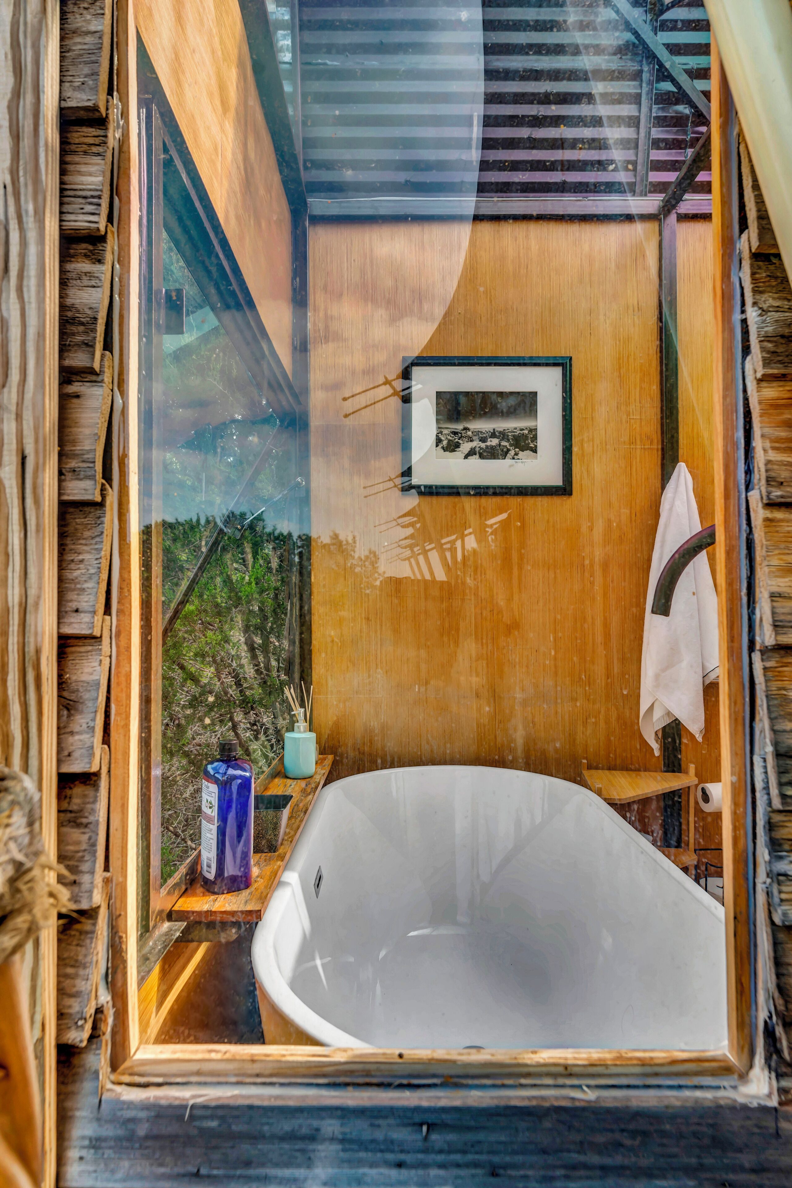 A bathroom with a bathtub, wooden walls, a framed picture, and a towel hanging on the wall.