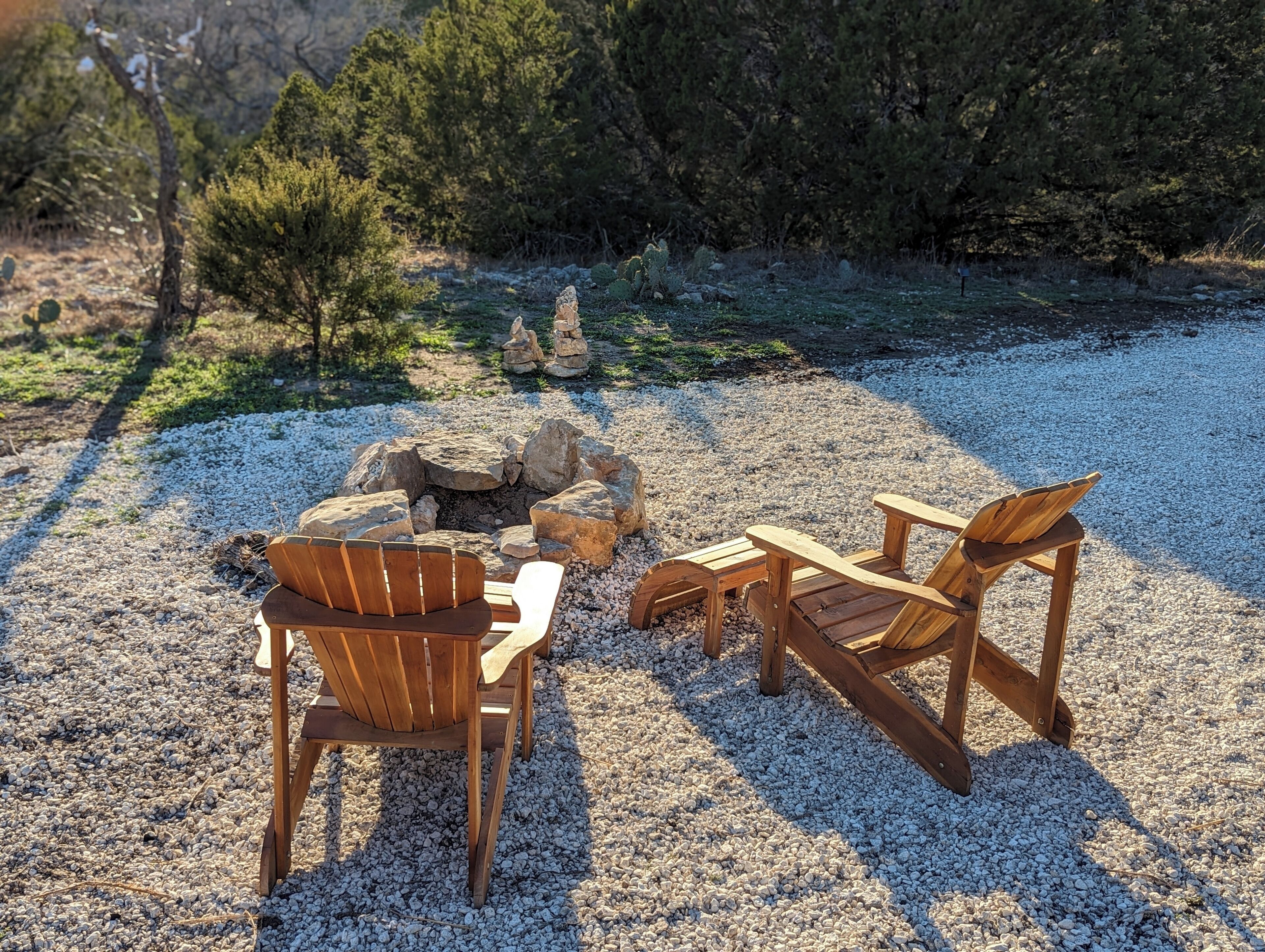 Un espacio al aire libre rústico con sillas de madera y un hogar de piedra rodeado de grava.