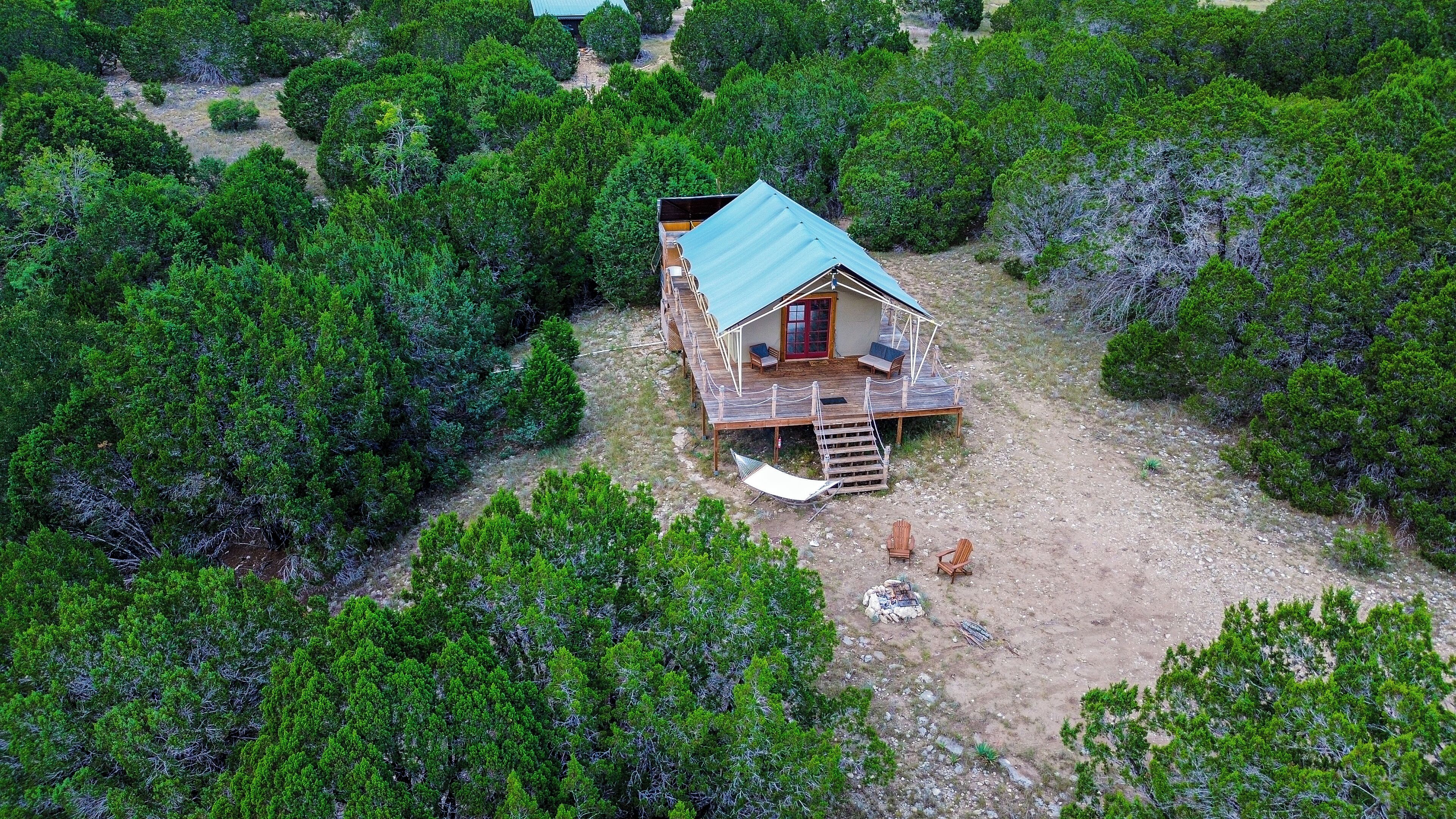 An aerial view of a wooden cabin with a deck, surrounded by dense greenery.