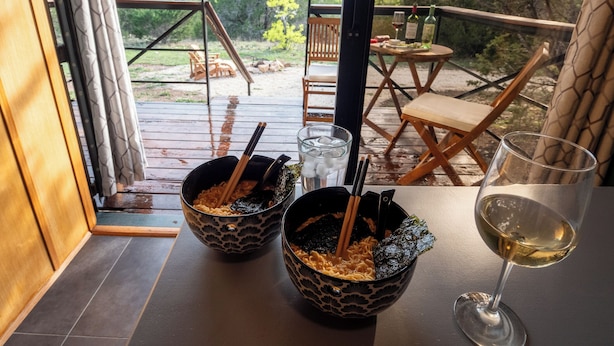 A dining area with two bowls of ramen and a glass of white wine on a table. - Lost Horizon Texas (Kempner)