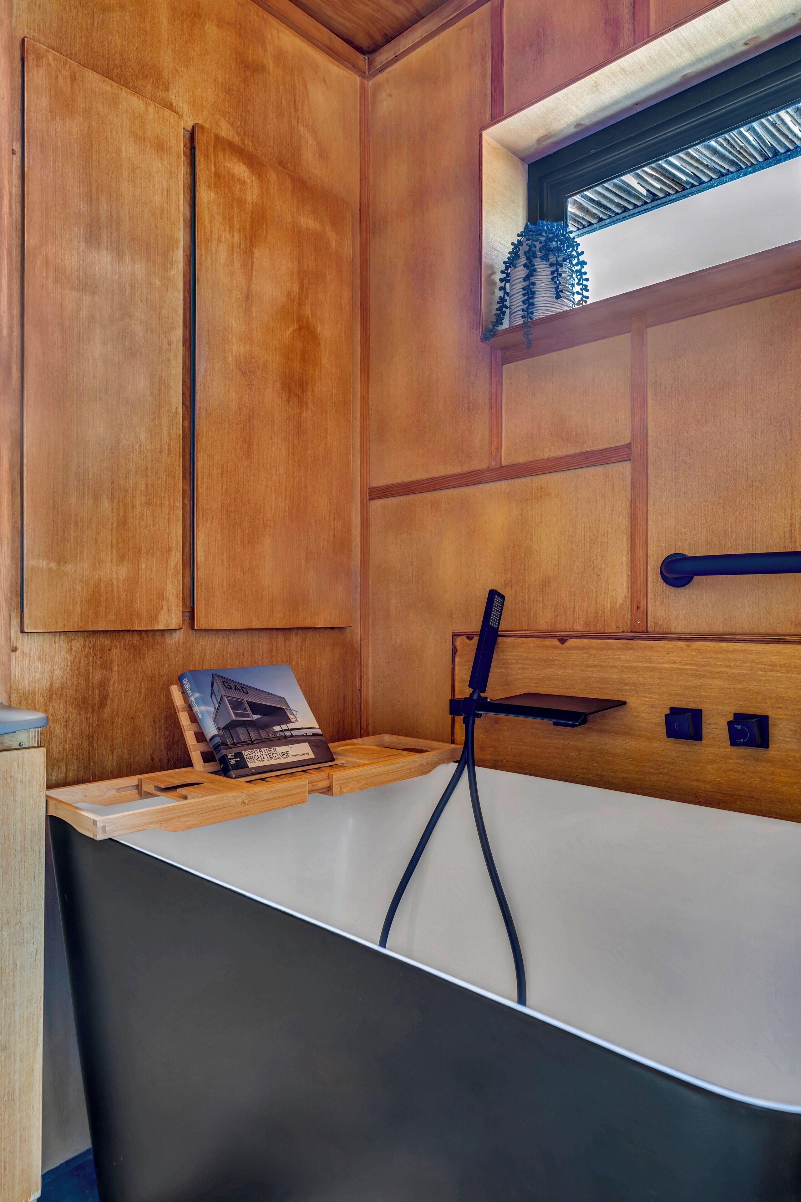 A modern bathroom with wooden paneling, a freestanding bathtub, and a small window with a decorative plant.