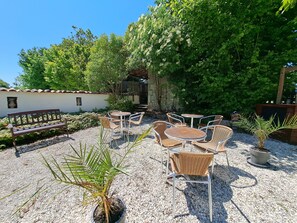 Relax in a serene outdoor space surrounded by lush greenery and trees, with comfortable seating and tables.