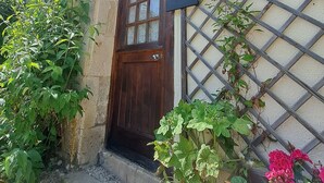 A rustic building with a wooden door, a window with a sign above it, and a lattice window. There are plants and flowers in front of the building. - 'Horloge' La Grange du Moulin - Exclusively families, heated pool, garden, wifi (Saint-Pierre-de-Juillers)