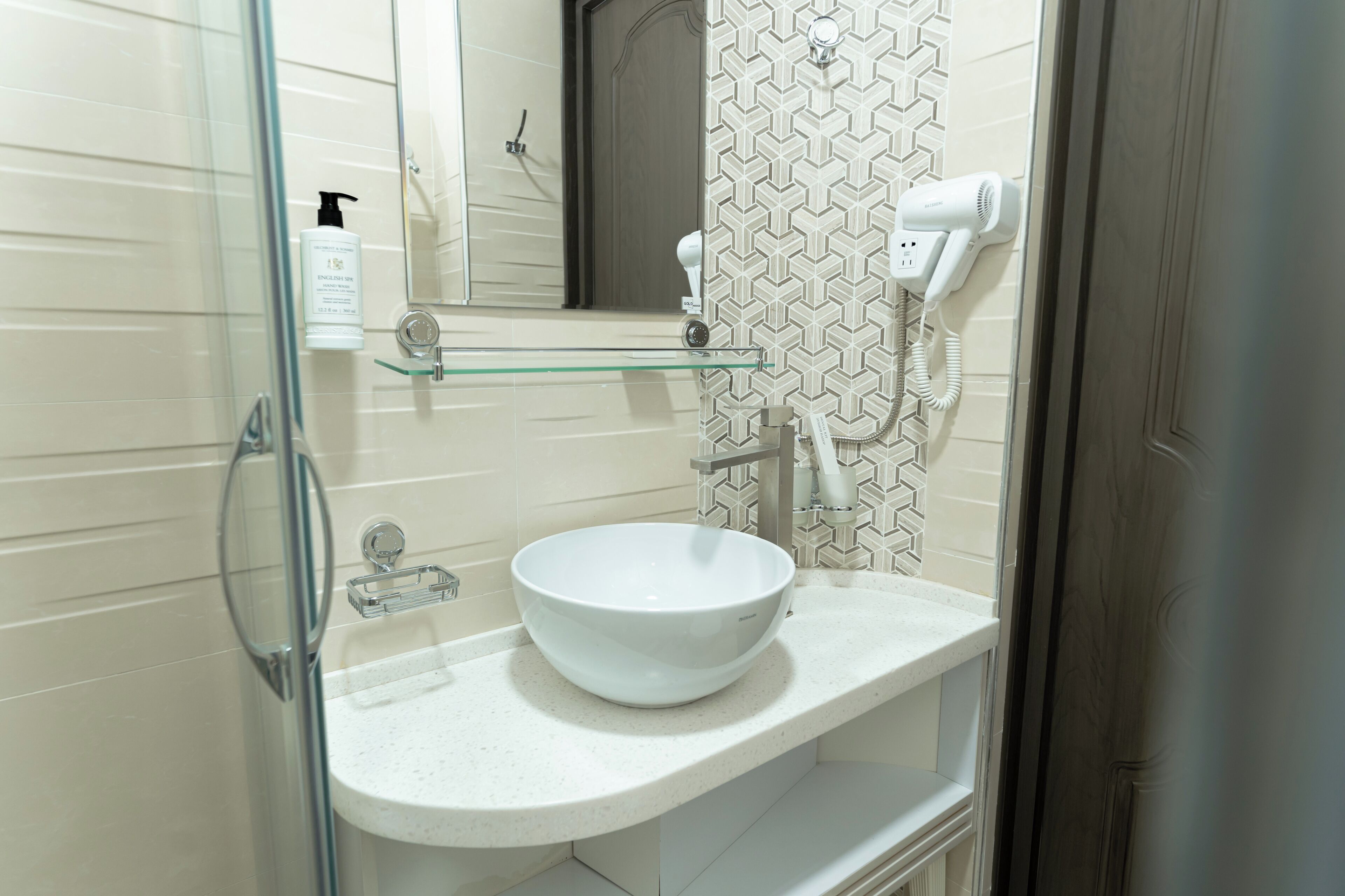 A bathroom with a white sink, a glass shower enclosure, a hairdryer, and a towel rack.