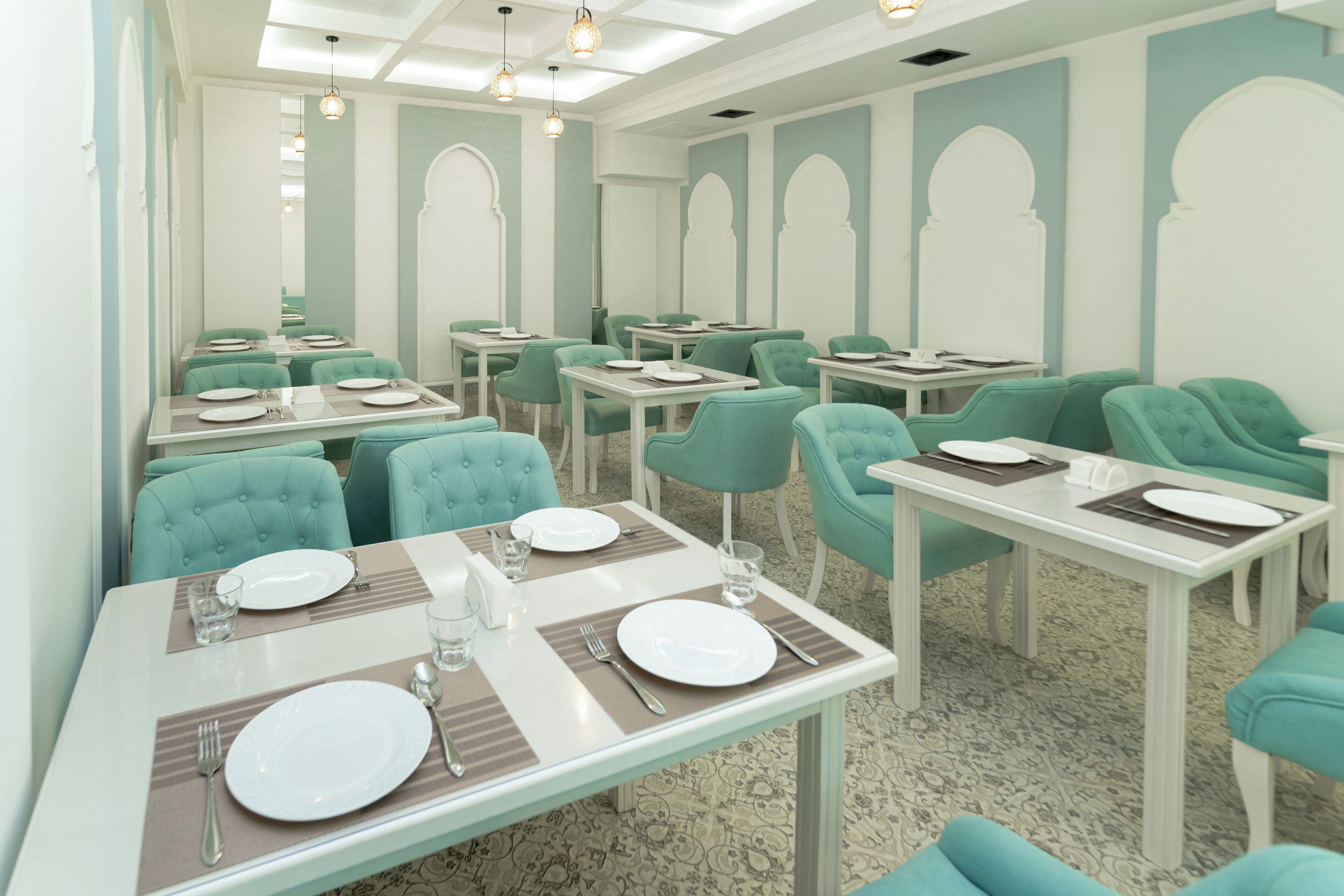A restaurant with teal chairs and white tables, each set with plates, cutlery, and glasses.