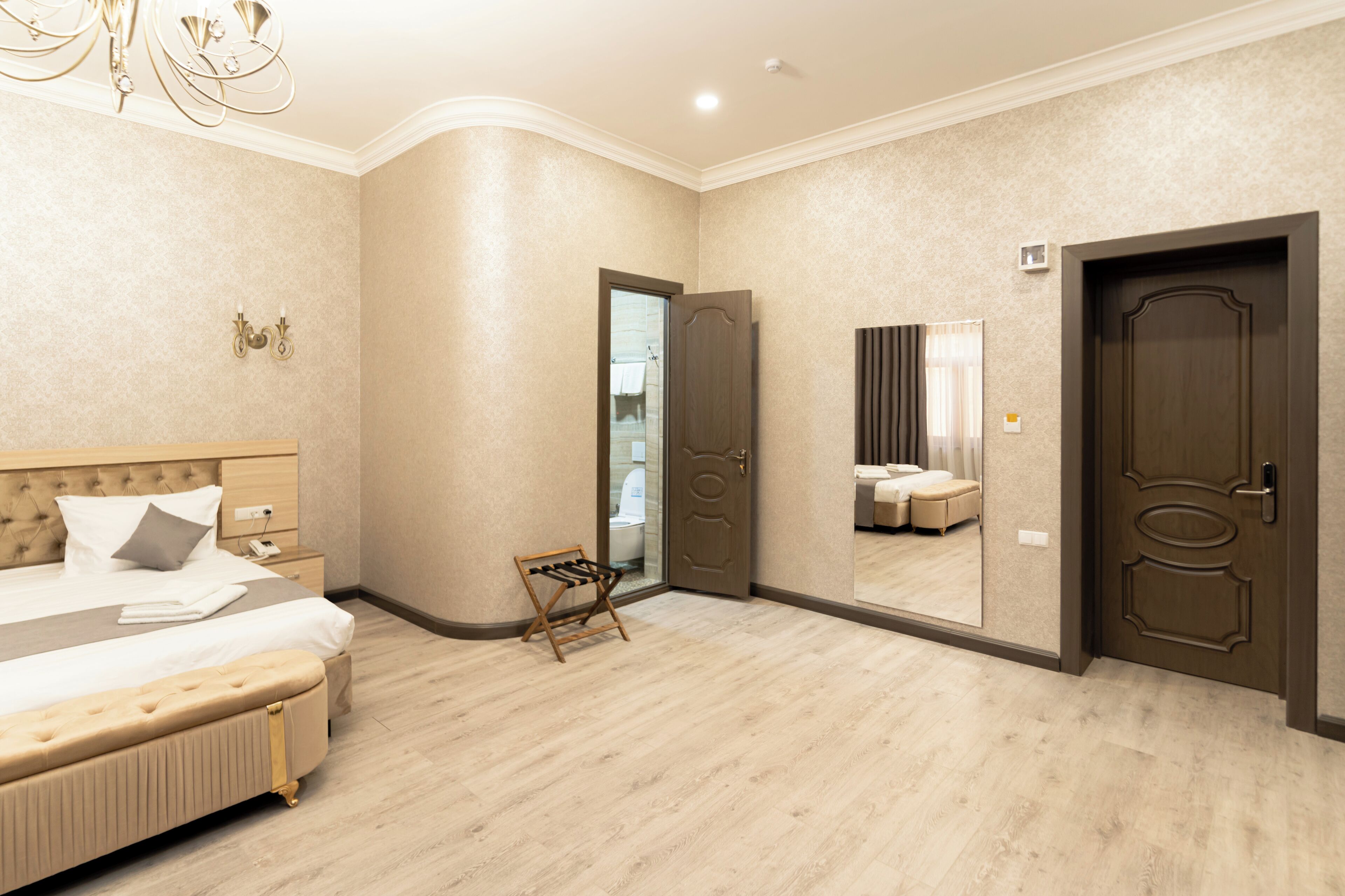 A hotel room with a large bed, a wooden bench, a mirror, and a door leading to a bathroom.