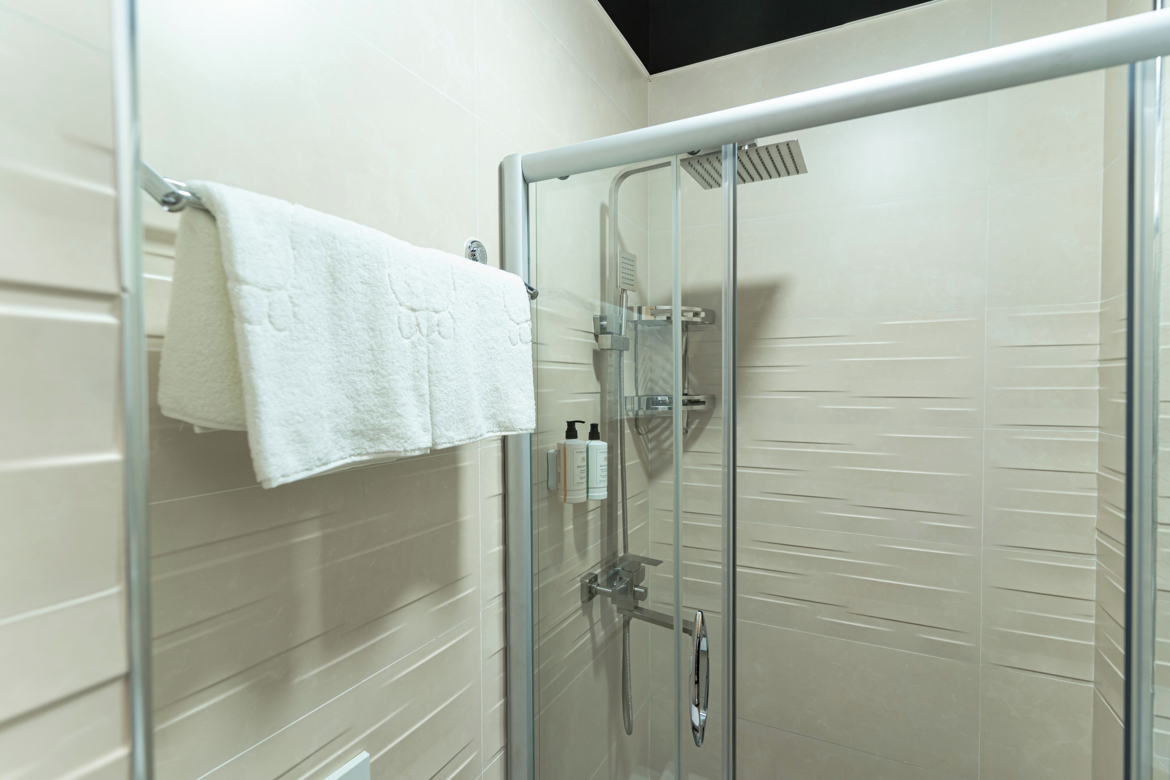 Une douche fermée par des parois de verre, avec une serviette blanche suspendue à un porte-serviettes en métal.