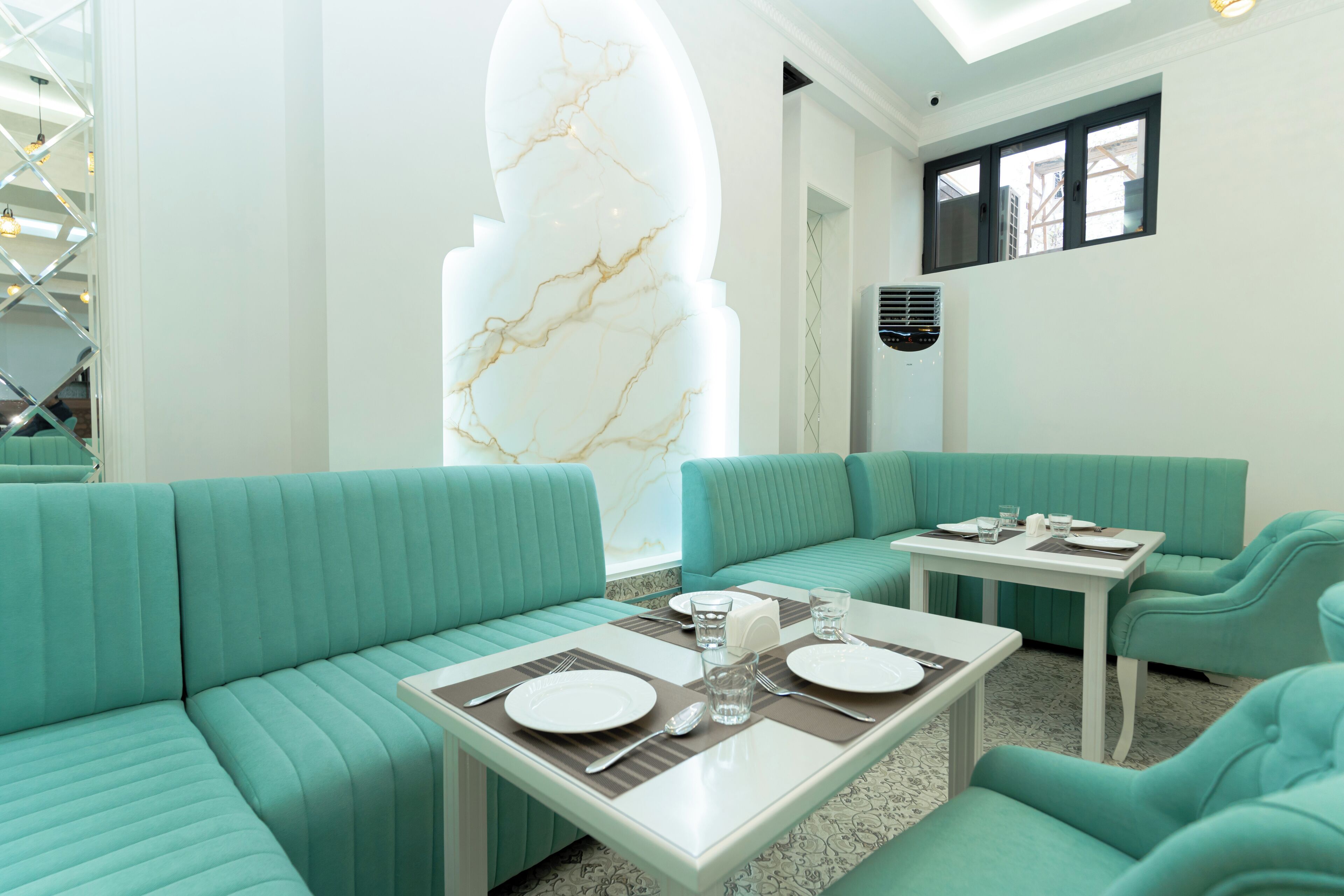 A teal-colored seating area with a marble accent wall, a white table set for dining, and a modern air conditioning unit.