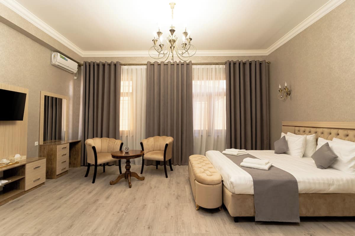 A hotel room with a bed, a TV, a desk, two chairs, and a chandelier.