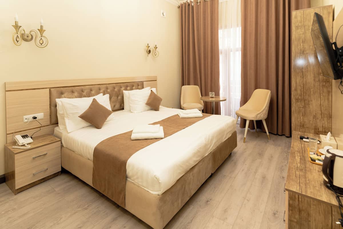 A hotel room with a large bed, bedside tables, a desk, a chair, and a TV.