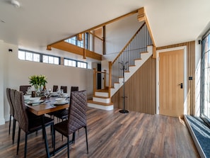 A modern dining area with a wooden table, leather chairs, and a staircase with wooden railings. - Stable View Barn - UK45938 (Corley)
