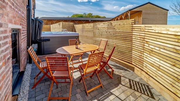 Een terras met een jacuzzi, houten stoelen en een tafel.