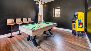 Een pooltafel met stoelen, een klein raam en een kleurrijke automaat.