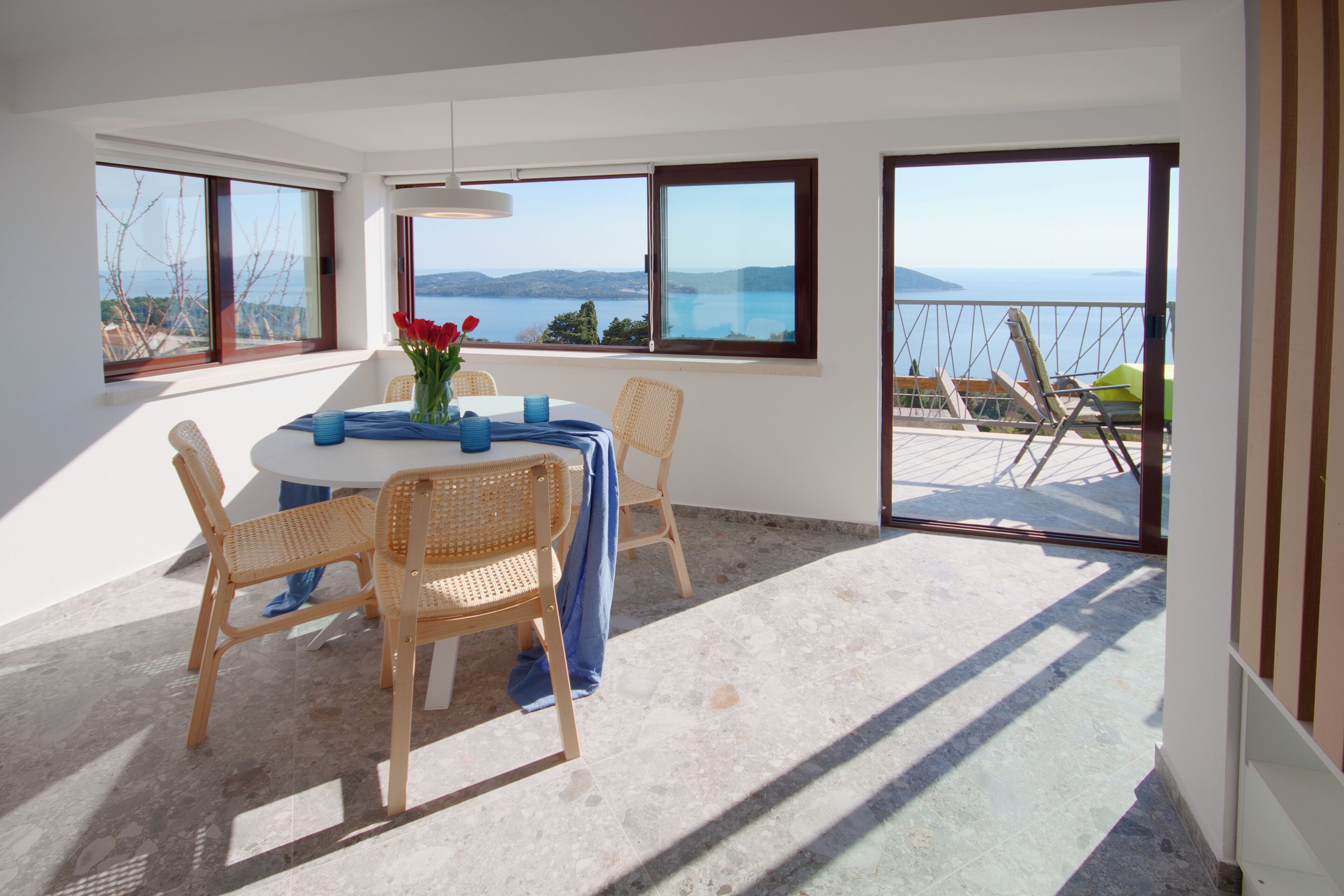 A dining area with a table, chairs, and a view of the sea through large windows.