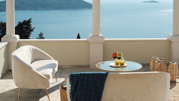 A balcony with a view of the sea, a round table with drinks, a white armchair, and wicker vases. - Villa Judita Dubrovnik (Dubrovnik)