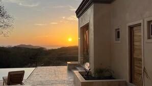 A patio with a view of the sunset, a wooden chair, and a small table. - Surf, Sun, Serenity! Luxury Private NEW Villa w/ Pool, Ocean and Valley Views.  (San Juan del Sur)