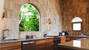A modern kitchen with a large island, wooden cabinetry, and a view of greenery through an arched window. - Surf, Sun, Serenity! Luxury Private NEW Villa w/ Pool, Ocean and Valley Views.  (San Juan del Sur)